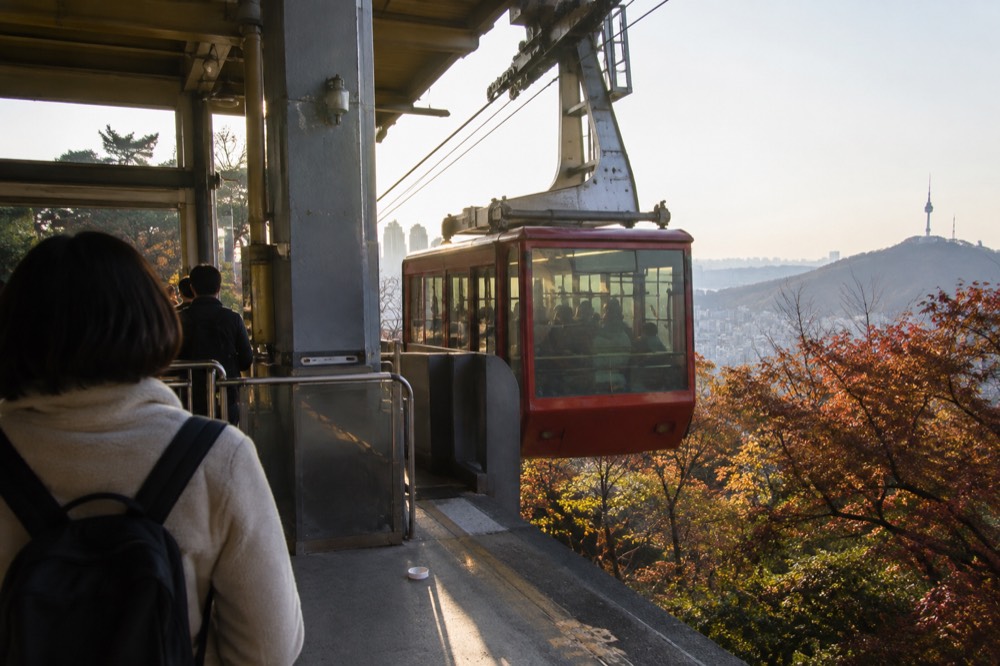 Red cable car cabins arriving at the upper station on the forested Namsan summit