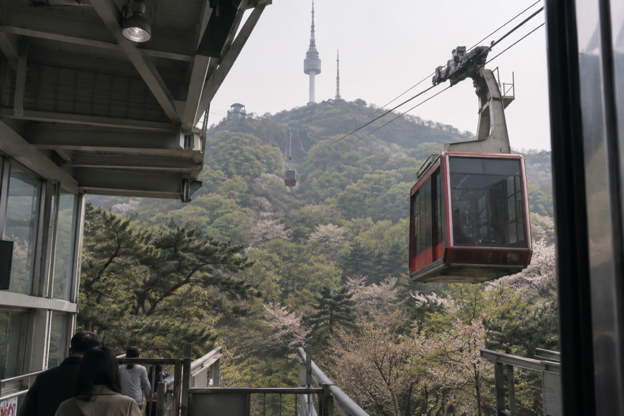 Red cable car cabins travelling up the forested slope of Namsan toward the tower on the summit