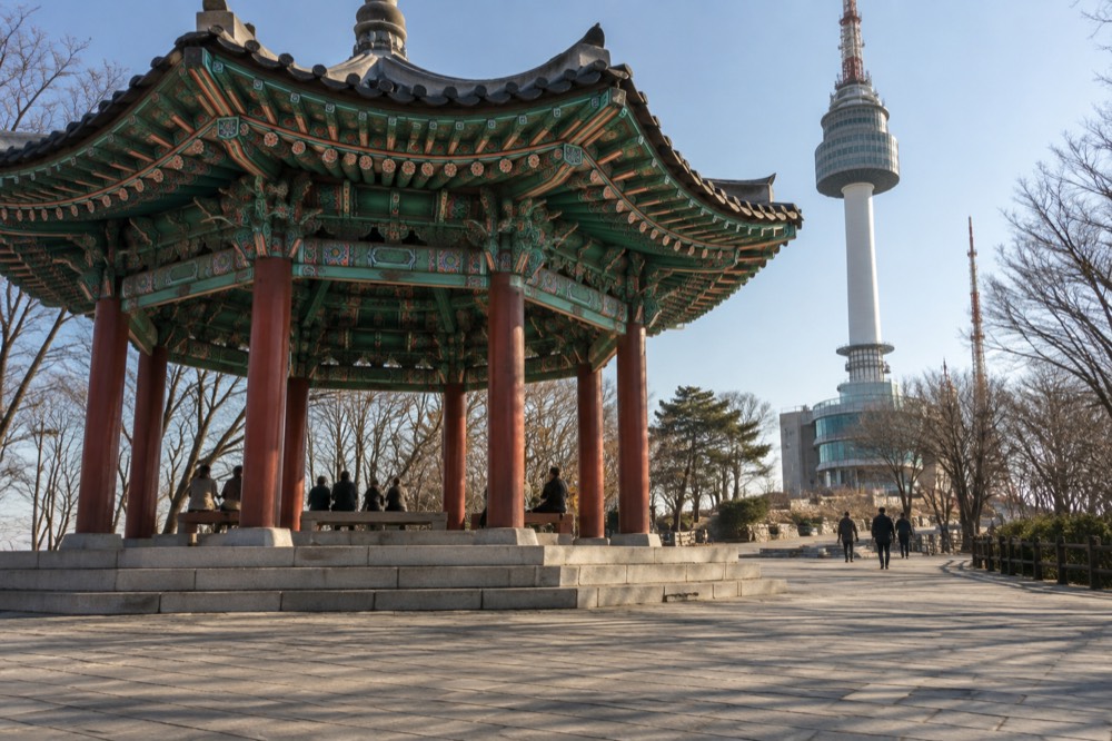 Palgakjeong pavilion and the tower base plaza with visitors walking on a clear day