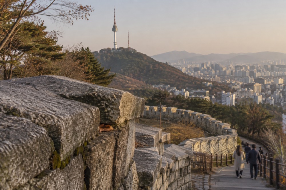 A stone section of the Seoul City Wall with N Seoul Tower in the background and the city beyond