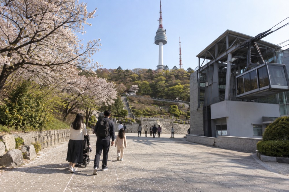Visitors walking toward N Seoul Tower across the summit plaza with the tower rising ahead