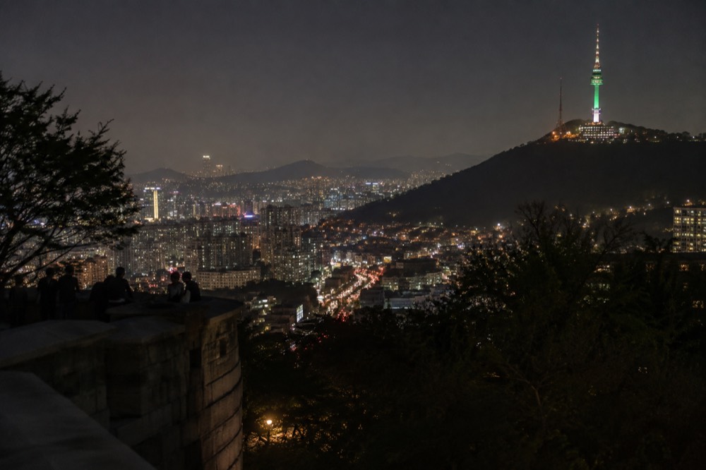 Night cityscape with rivers of light between dark hills and a glowing tower in the distance