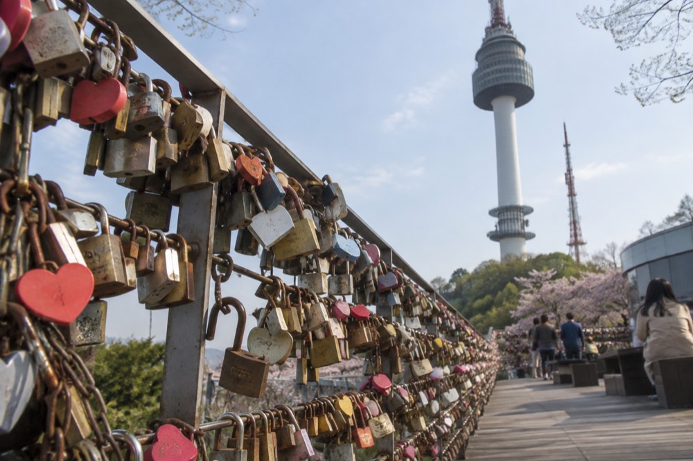 Rows of padlocks attached to railings on the Namsan love lock deck, with the tower behind
