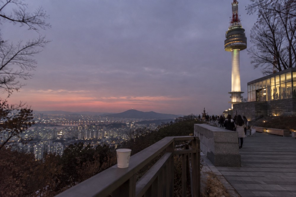 A wide view of the Namsan summit at dusk, with the illuminated tower and the city skyline glowing below