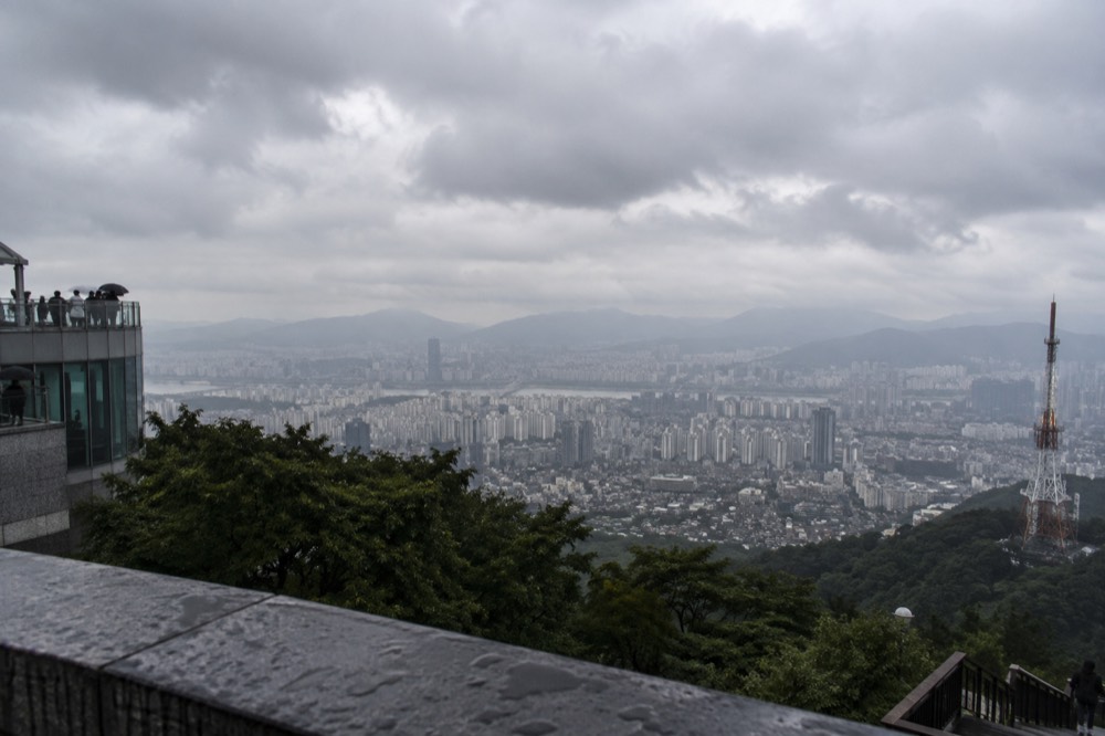 Grey monsoon clouds over a dense Seoul skyline with hills in the distance