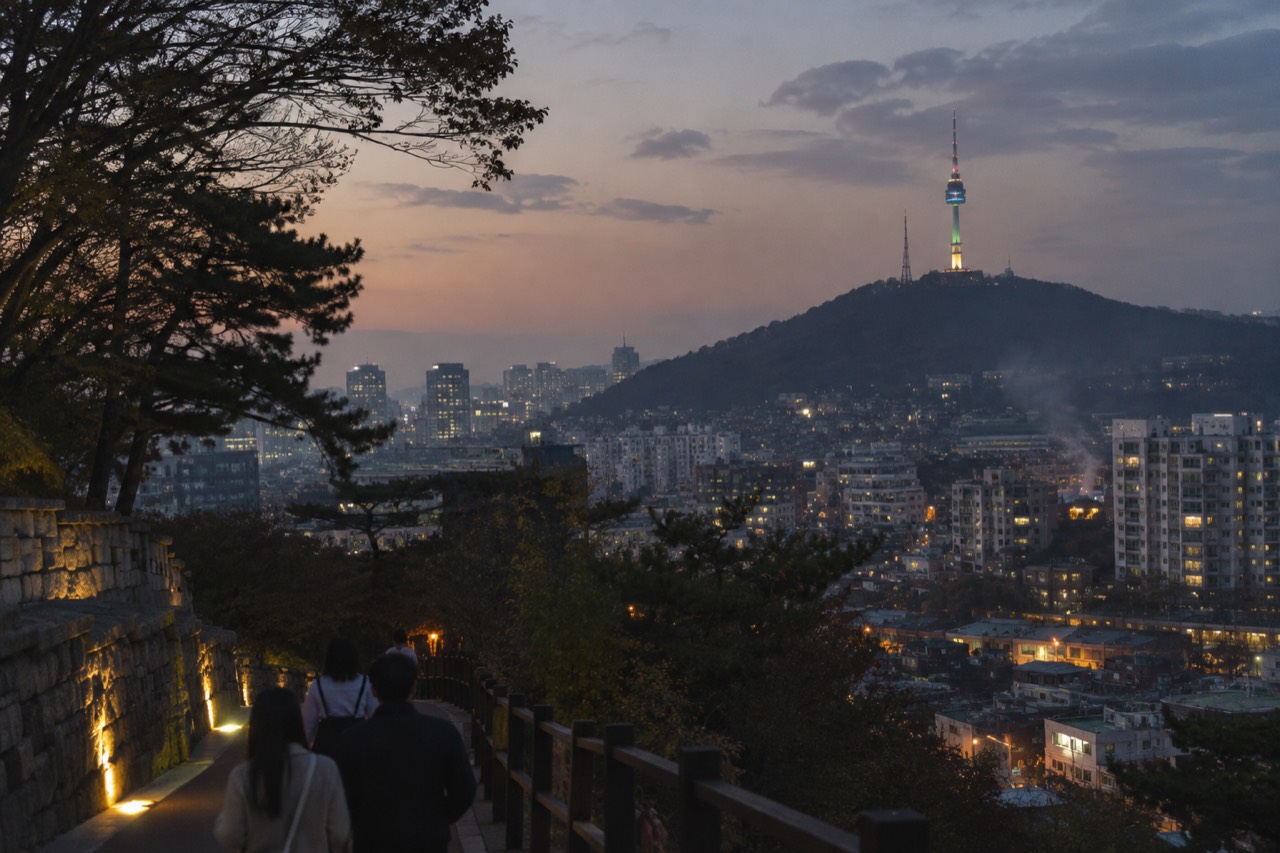Evening view of Seoul skyline with a lit communications tower on a forested hill above apartment blocks