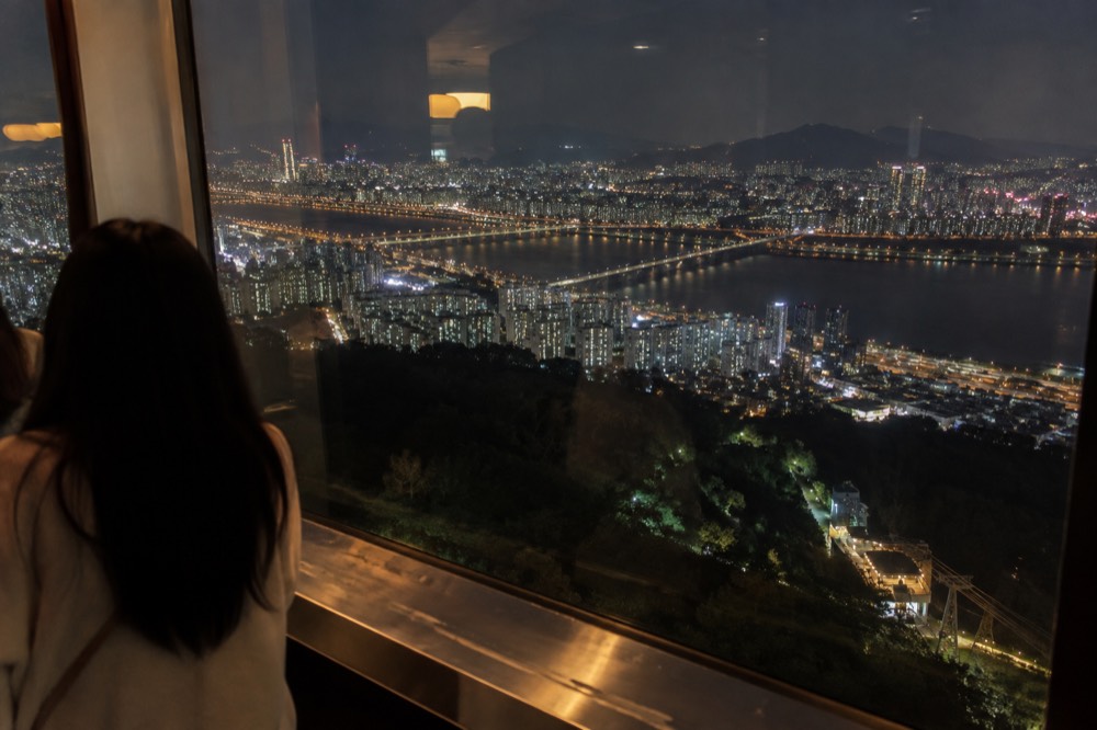 Seoul's night skyline seen from a high observation deck, with the Han River winding through fields of city lights