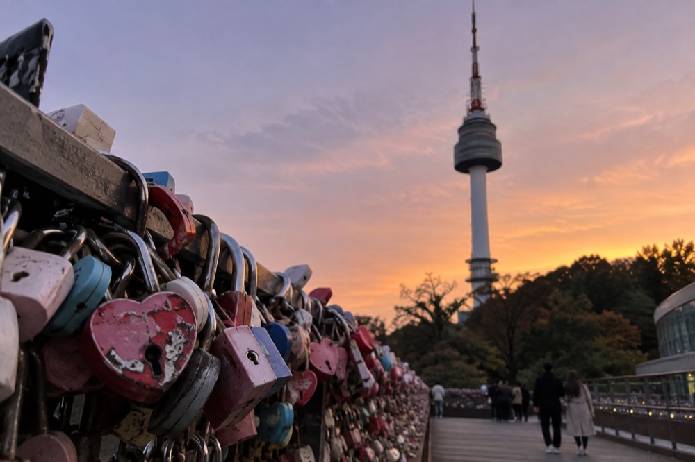 A padlock railing in the foreground with a communications tower and evening sky behind