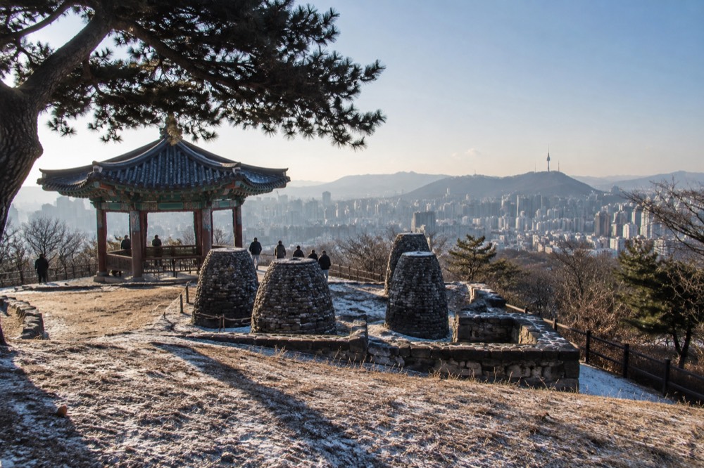 Pavilion and stone beacon mound on a wooded hilltop above city rooftops