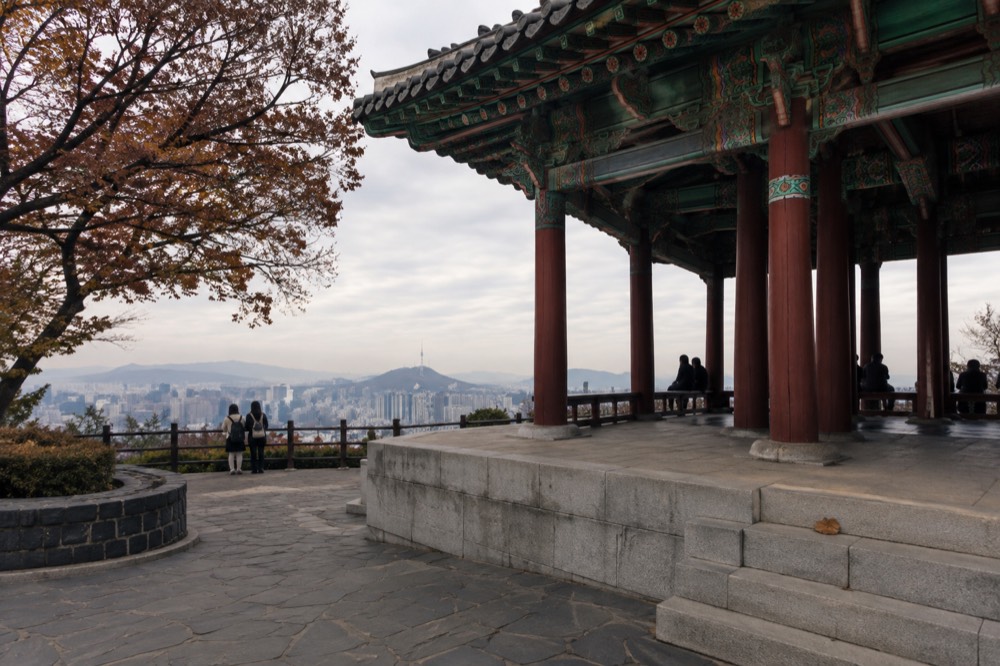 A traditional wooden pavilion on a summit plaza with the city spreading out below