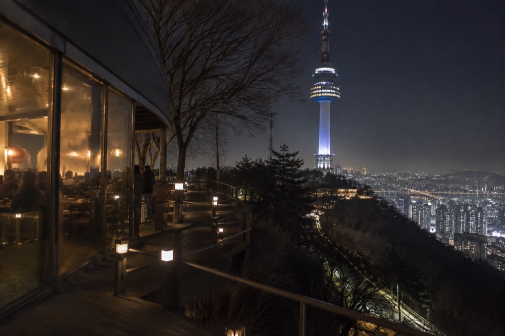 Night view from a summit terrace with restaurant windows glowing and city lights below