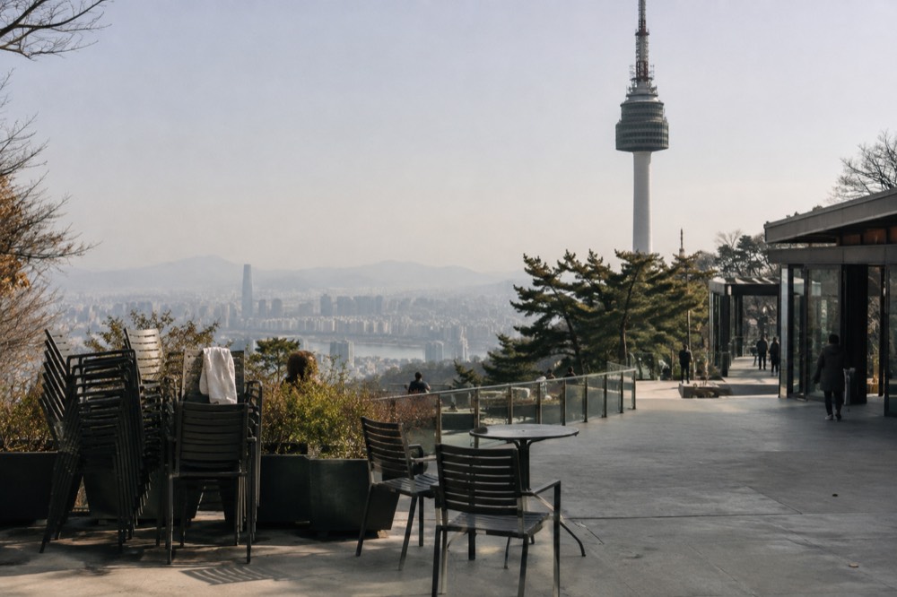 The summit plaza surrounding the base of N Seoul Tower with terrace seating and the city skyline beyond