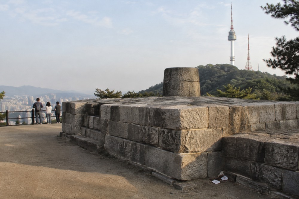 A restored stone beacon platform on a hilltop with a modern tower rising behind it