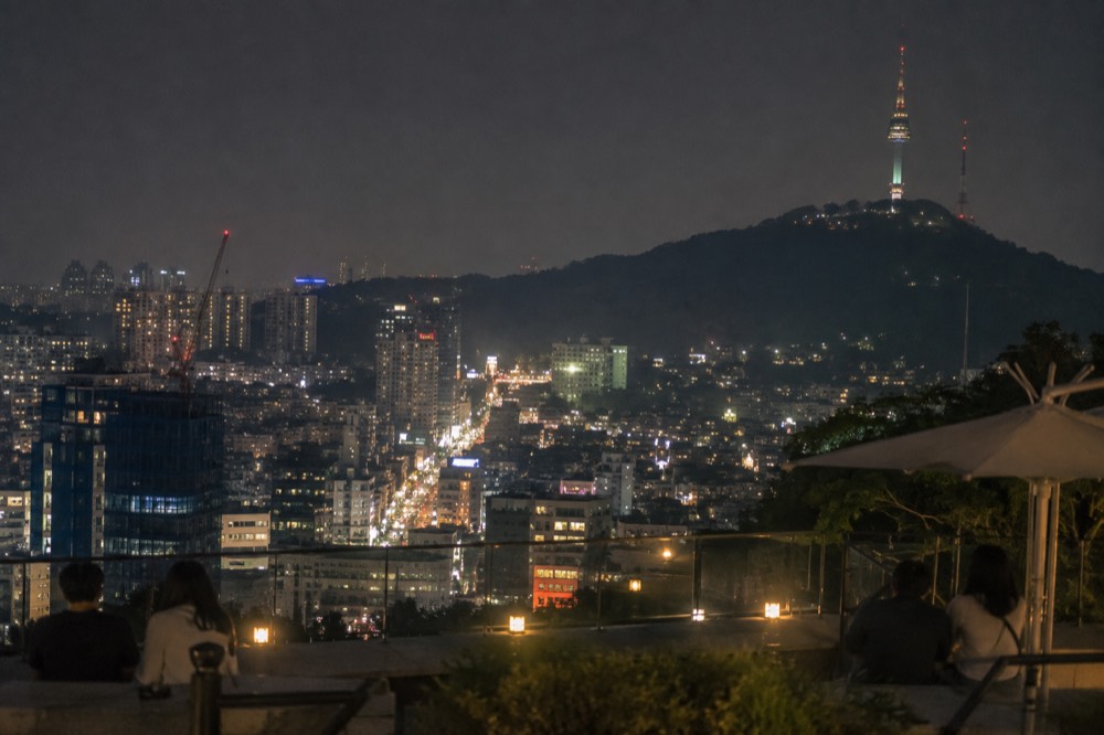 Night view over a dense city with a illuminated tower on a hill