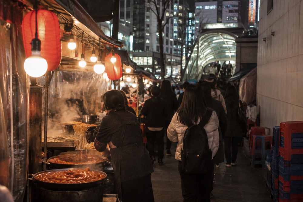 Night market alley glowing with food stall lights and hanging lanterns above crowded stalls