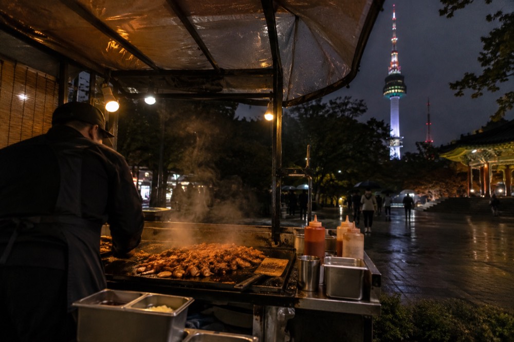Food stall at night with steam rising from a hot griddle and warm stall lights