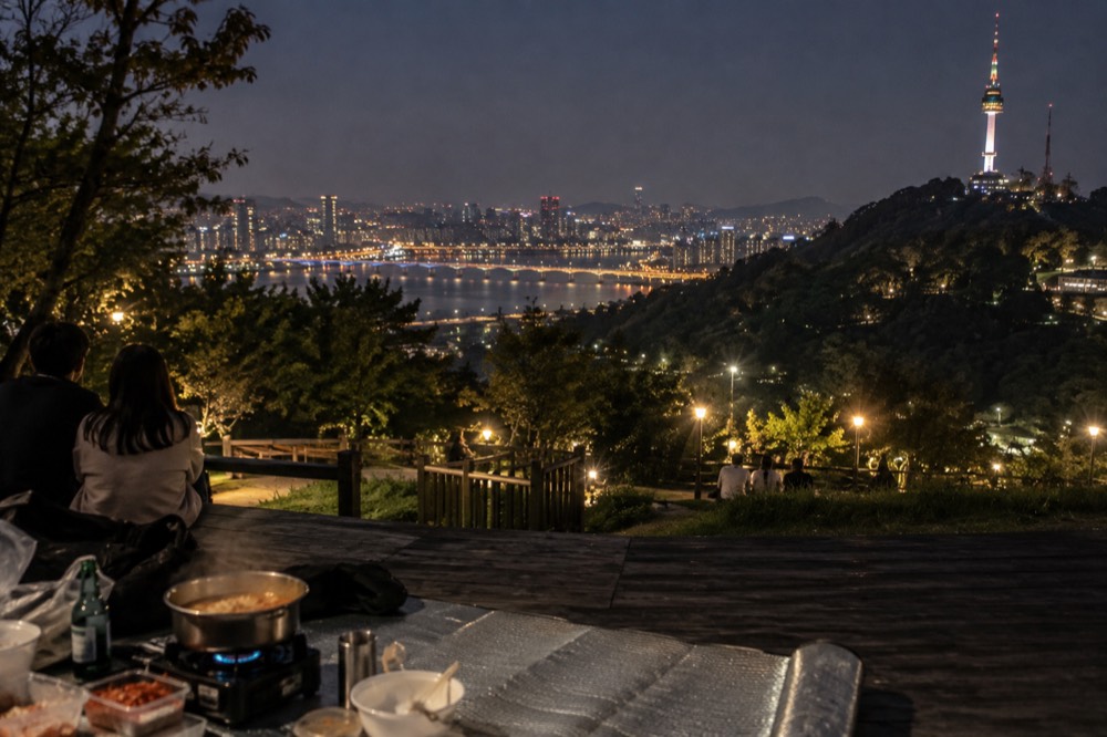 Lit bridge arching over a wide dark river with park lights along the bank