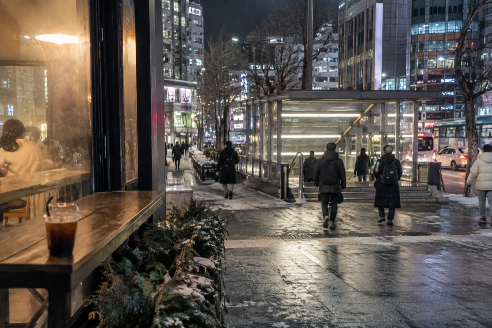 City street at night with warm cafe lights and reflections on a cold pavement