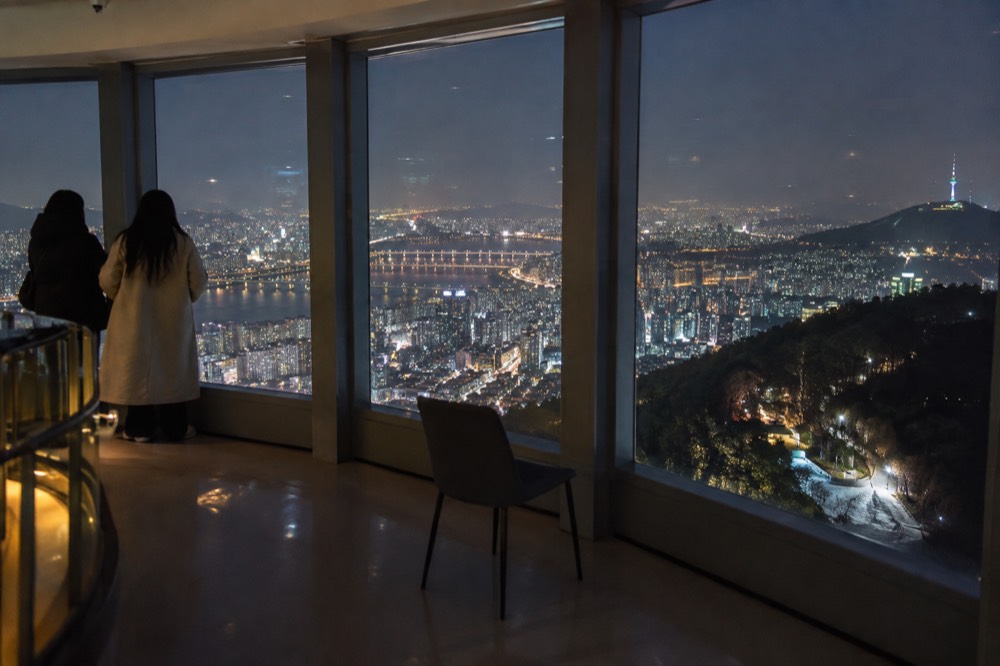 A glass-walled observation deck interior at night with a city spreading in lights below